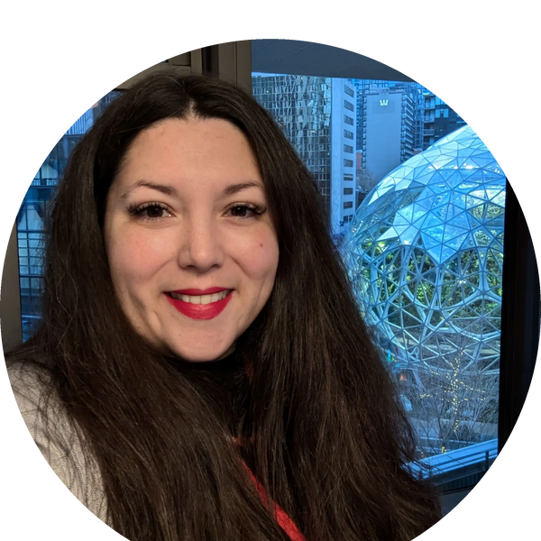 Smiling woman with long dark hair in front of a glass dome and cityscape.
