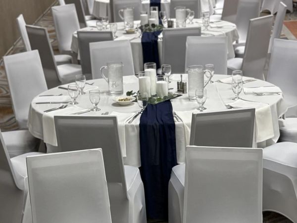 Elegant round tables with white covers and blue runners set for an event.