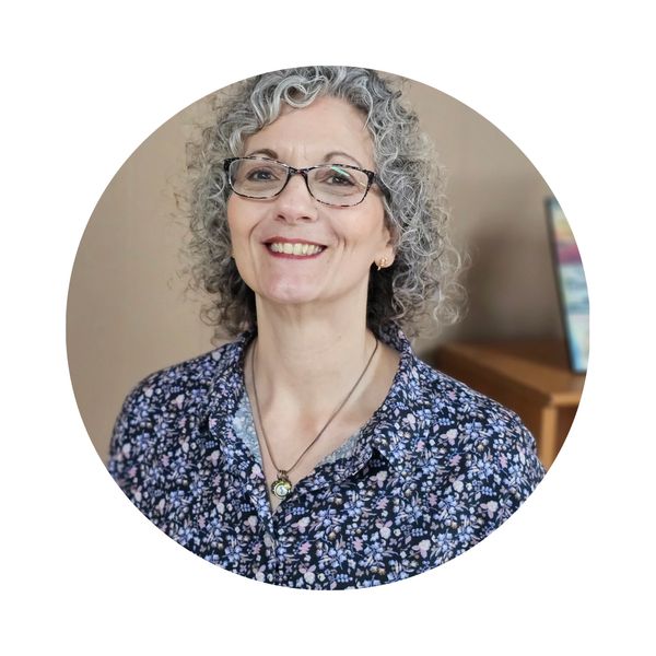Smiling woman with curly gray hair and glasses.
