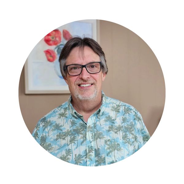 Smiling man wearing glasses and a palm tree patterned shirt.