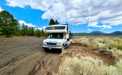 RV parked in a scenic open field near trees and hills.