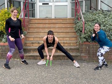Three women in workout attire posing outdoors in front of stairs.