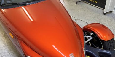 Shiny orange three-wheeled car in a garage with MCB Motor Spa sign.