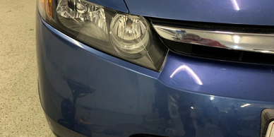 Close-up of a blue car's front headlight and bumper in a garage.