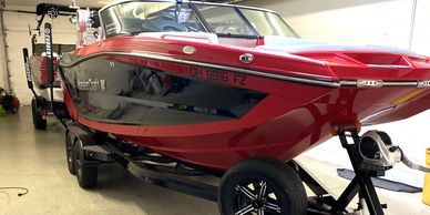 Red and black wakeboard boat on a trailer indoors.
