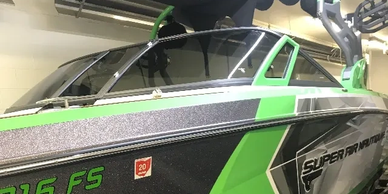 Green and black wakeboard boat with tower and bimini top on trailer indoors.