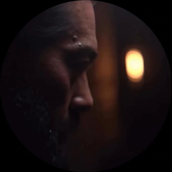 Profile of a bearded man in dim light with a glowing background.