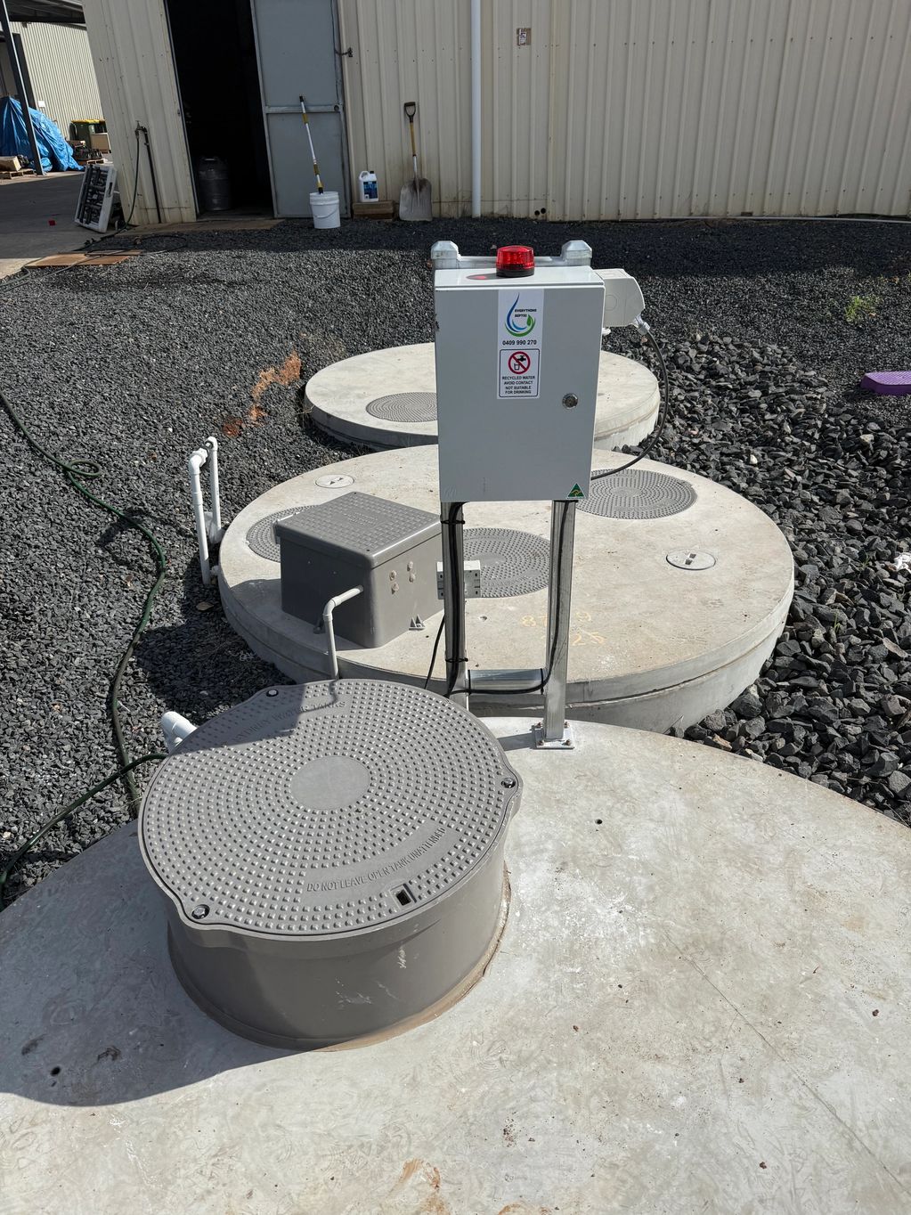 Three large concrete tanks with lids and a control box outside a building.