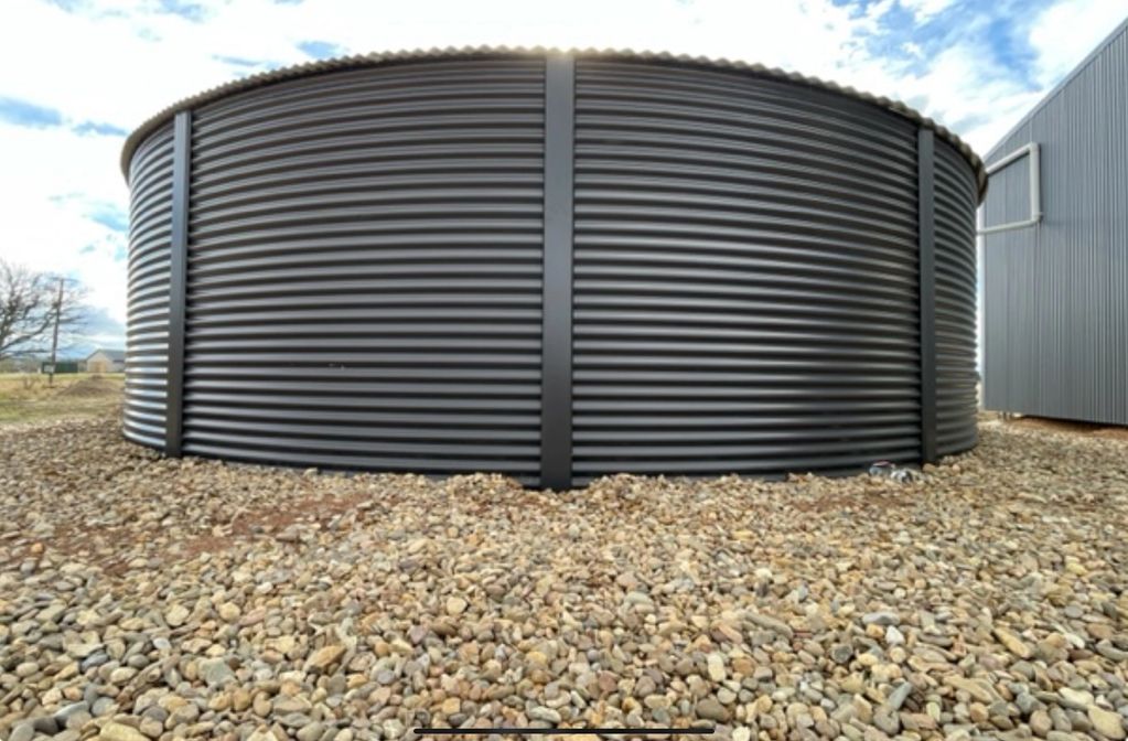Large black corrugated metal water tank on rocky ground.
