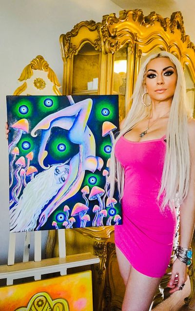 Jameela, the Divine Visionary Artist, holds her painting Twilight's Guardian, of a mystical fairy.