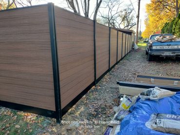 Newly installed brown composite fence with black aluminum posts beside a parked pickup truck.