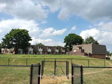 Residential buildings behind a fenced grassy area under a partly cloudy sky.