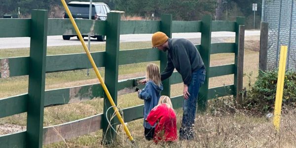 A man and two children painting a wooden fence outdoors.