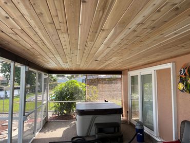 Covered patio with wooden ceiling and hot tub overlooking a garden and canal.
