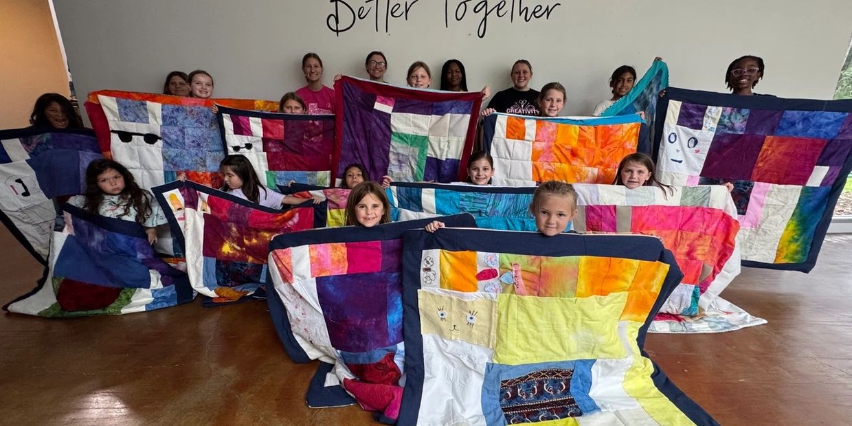 Group of children proudly displaying colorful patchwork quilts indoors.