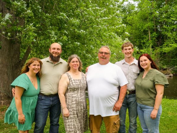 A happy family posing outdoors in a green, leafy setting.