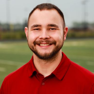 Smiling man in red sports polo with eagle logo on a field.