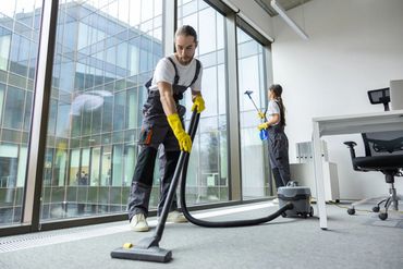 Two workers cleaning a modern office with vacuum and spray.