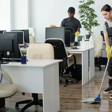 Two janitors cleaning an office with a wet floor sign.