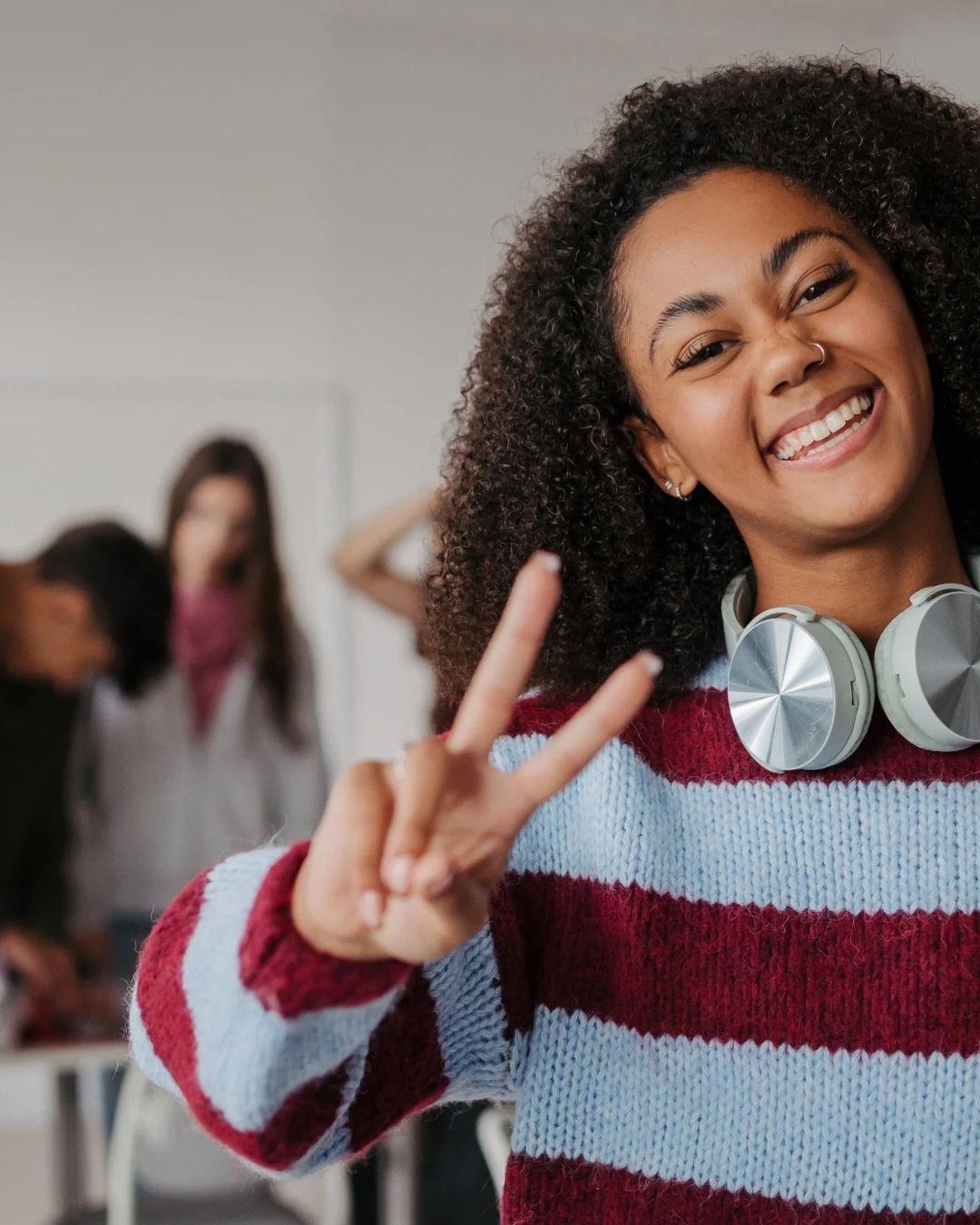 Smiling woman showing peace sign with headphones around her neck ready to start the HerAI Entrepreneurial track.