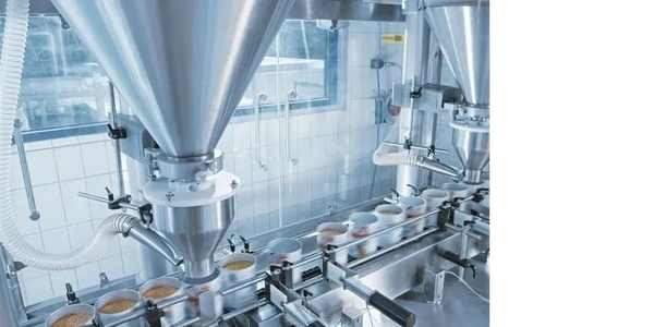 Automated machine filling cups with granular product in a clean industrial setting.