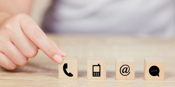 Hand pointing at wooden block with phone icons symbolizing communication methods.
