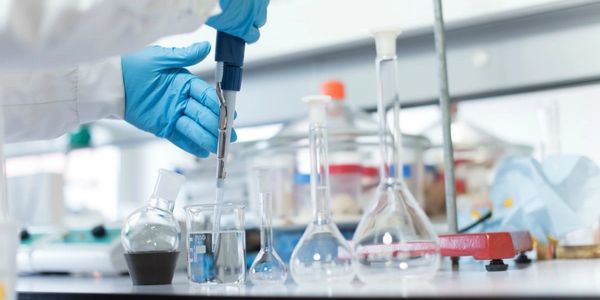 Scientist using a pipette in a laboratory with glassware on the bench.
