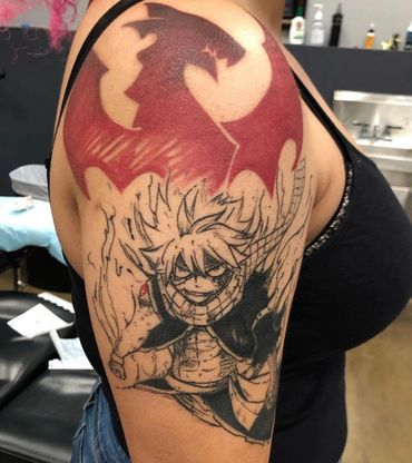 A detailed anime-themed tattoo with a fiery character and a red dragon emblem on the upper arm.