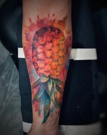 Vivid tattoo of a pineapple with watercolor effects on a forearm.