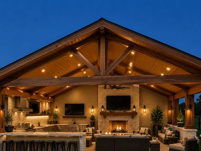 Cozy outdoor living area with fireplace and kitchen under wooden pavilion.