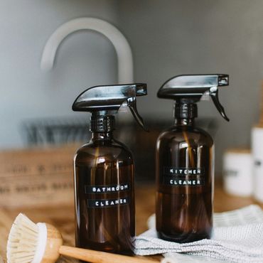 Two labeled spray bottles for bathroom and kitchen cleaning on a wooden surface.