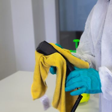 Person in protective gloves and suit cleaning a telephone receiver with a yellow cloth.
