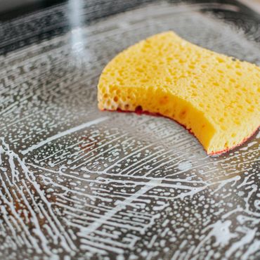 A yellow sponge with soap suds on a glass surface.