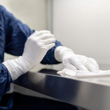 Person in protective gear sanitizing a metal surface with a cloth.