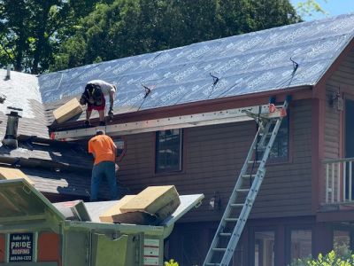 Two workers installing roofing materials on a house roof.