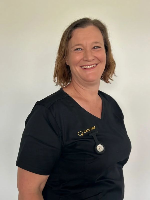 Smiling woman in black medical scrubs with a watch badge.