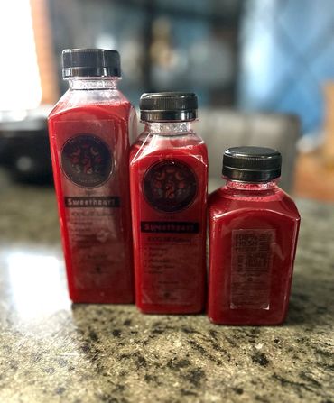 Three red juice bottles with black caps on a granite countertop.