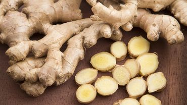 Fresh ginger roots with sliced pieces on a wooden surface.