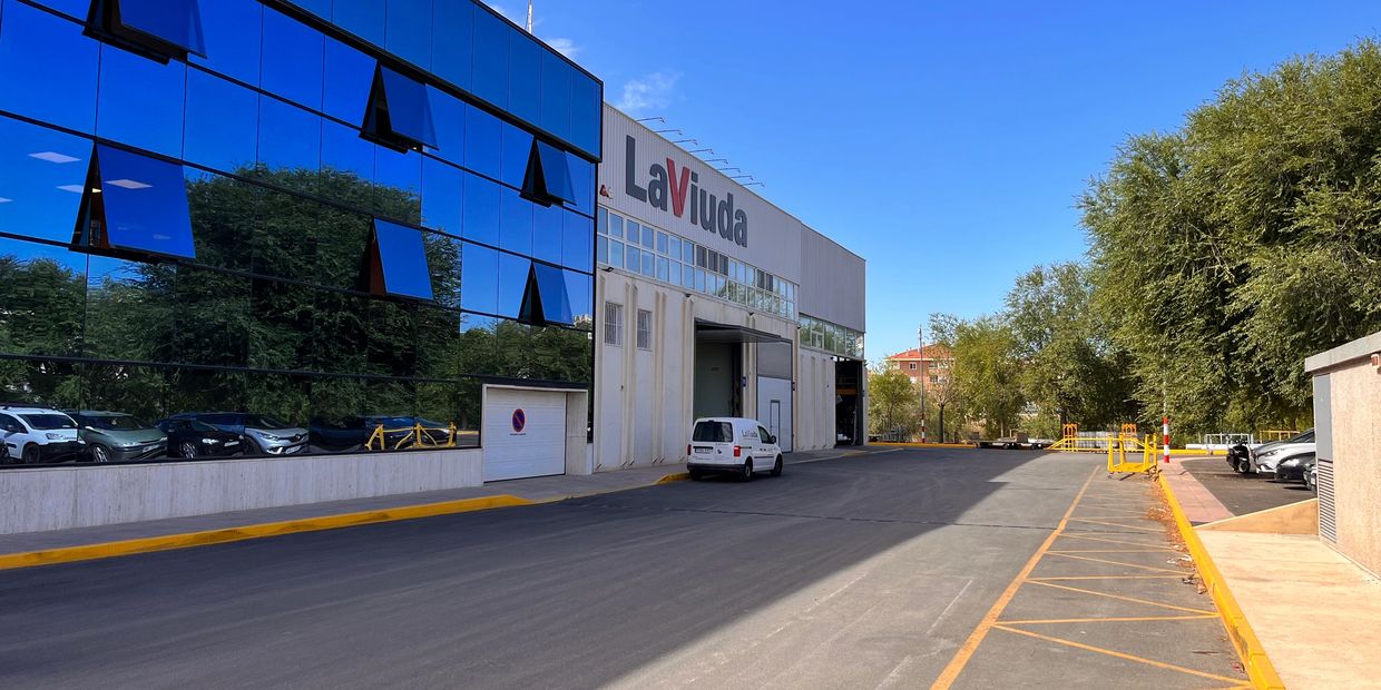 Modern building with reflective glass windows and a parking area on a clear day.