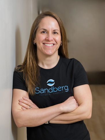 Smiling woman in a black Sandberg Physical Therapy t-shirt with arms crossed.
