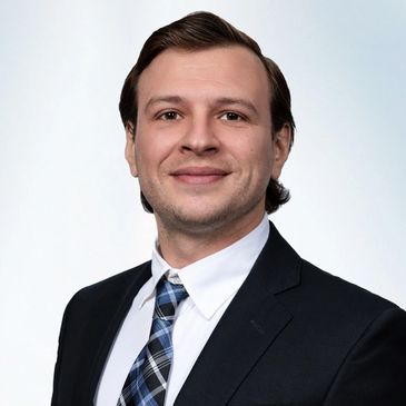 Professional man in a suit and tie smiling against a light background.