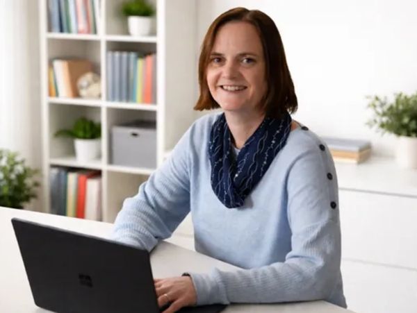 Smiling woman working on a laptop in a bright, organized office.
