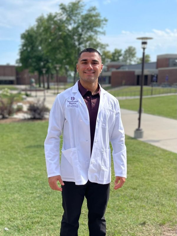 Man in a white lab coat outside on grass.