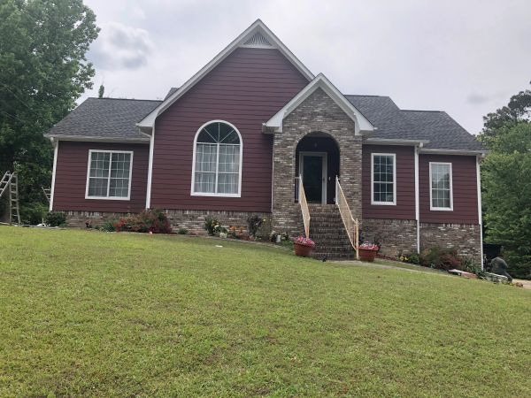 A red house with brick accents and a green lawn on a cloudy day.