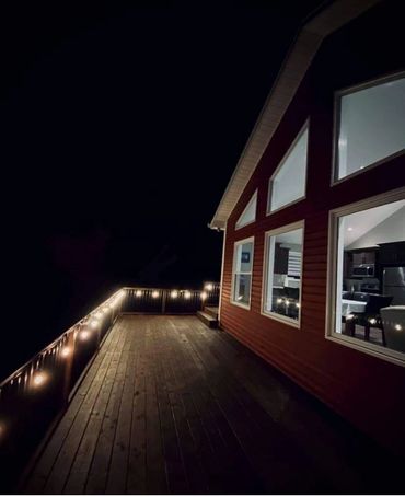 Red A Frame cabin with brown deck lit with patio lanterns from different angle.