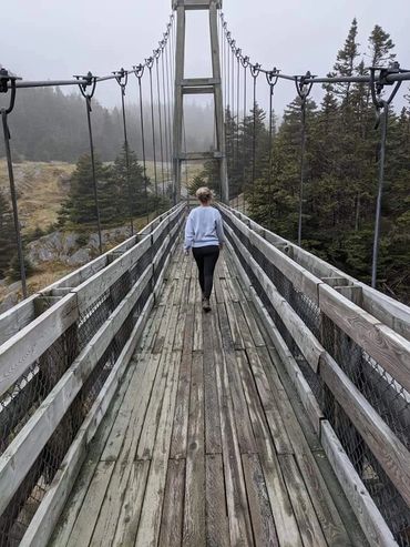 Woman in grey sweater and black pants standing on bridge in fog