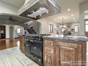 Open-concept kitchen with rich wood cabinetry, range hood, and a view to the staircase and living ar