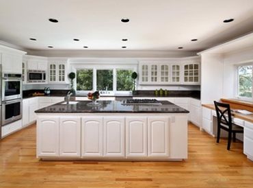 Kitchen with white painted cabinets, black granite countertops, and hardwood flooring - cabinet pain