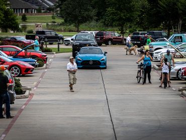People and cars gather in a parking lot, some with car hoods open.