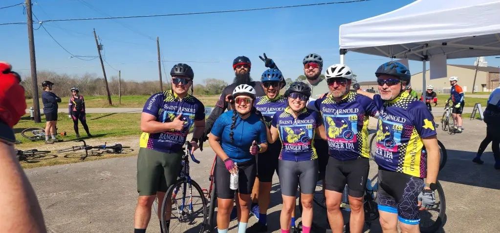 Group of cyclists posing happily in gear outdoors under a clear sky.